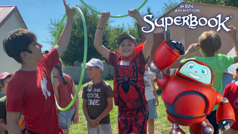 Mykhailo, a young boy in Ukraine, jumps up holding a hula hoop in his hands, while other members of the Superbook camp stand nearby. Gizmo stands in the foreground, smiling and raising his arm in the air. The CBN Animation and Superbook logos are stacked in the top right corner.